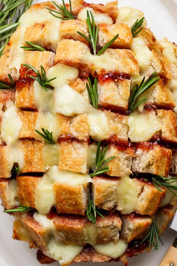 Top down shot of a cranberry brie pull apart loaf of bread cut into bite-sized pieces with rosemary.