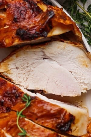 A plate with sliced deep fried turkey breast on it and fresh thyme next to it.