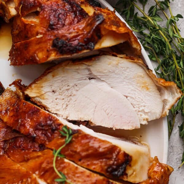 A plate with sliced deep fried turkey breast on it and fresh thyme next to it.