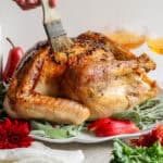 An Herbed Butter Turkey on a platter with red pears and herbs around it with someone basting the turkey with butter.