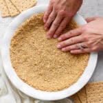 Top down shot of someone pressing a graham cracker crust into a pie plate.