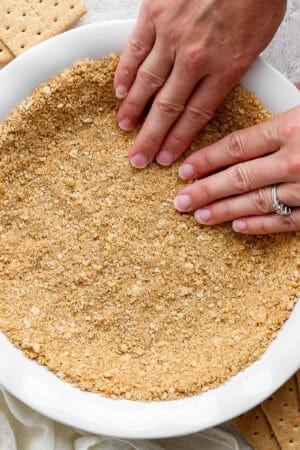 Top down shot of someone pressing a graham cracker crust into a pie plate.