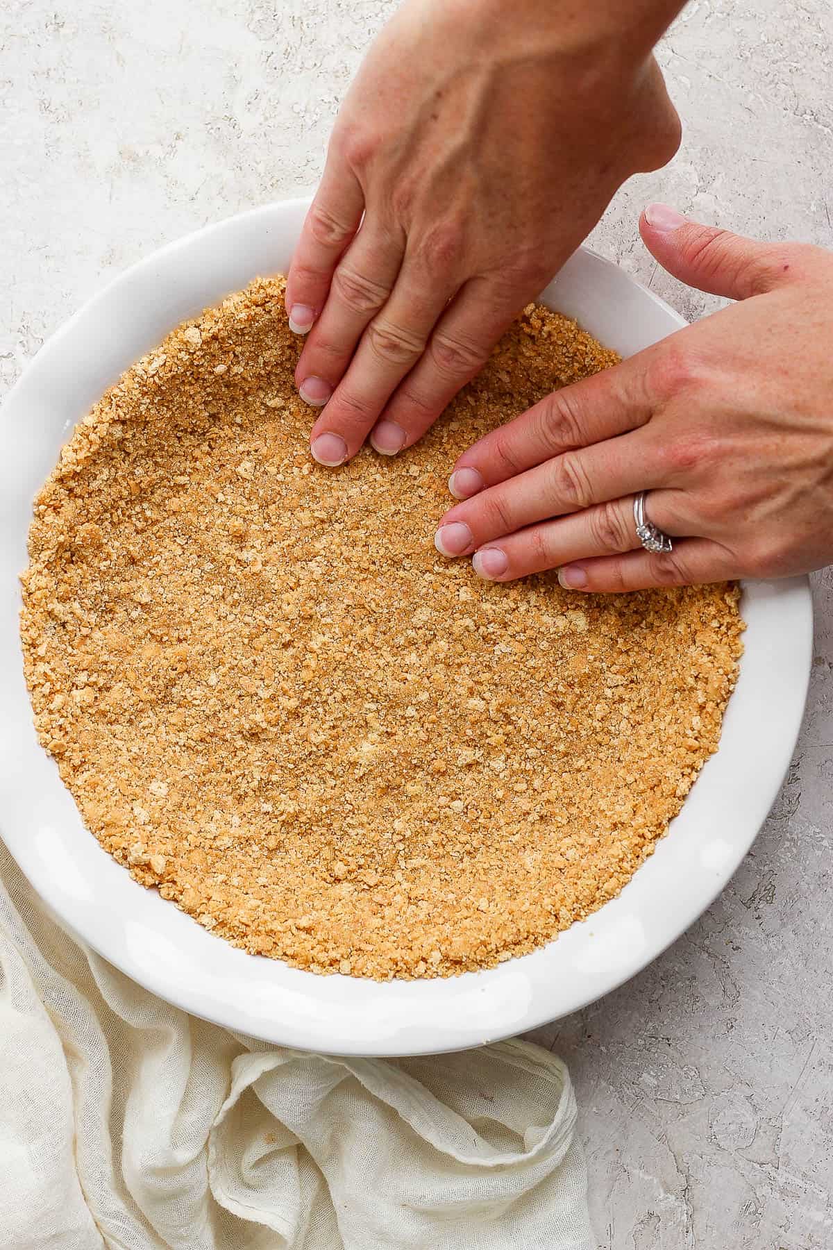 Two hands pressing the graham cracker crust into a pie pan.