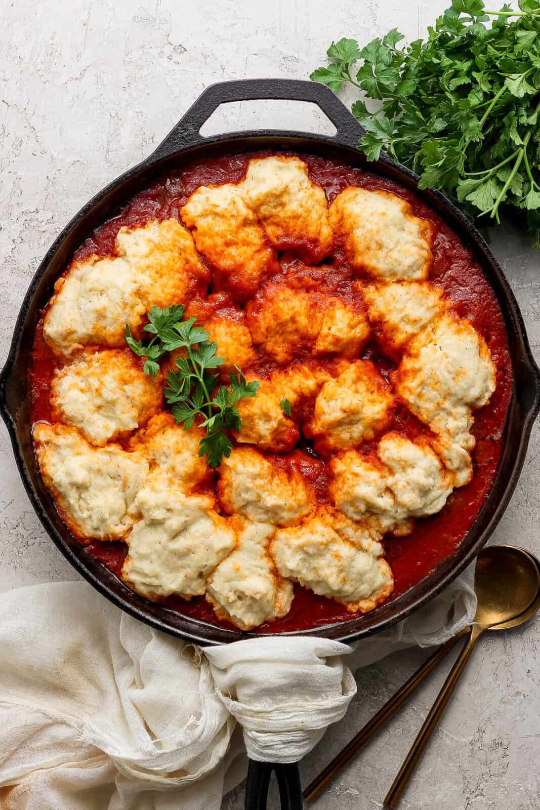 A cast iron skillet of meatballs and dumplings garnished with fresh parsley.