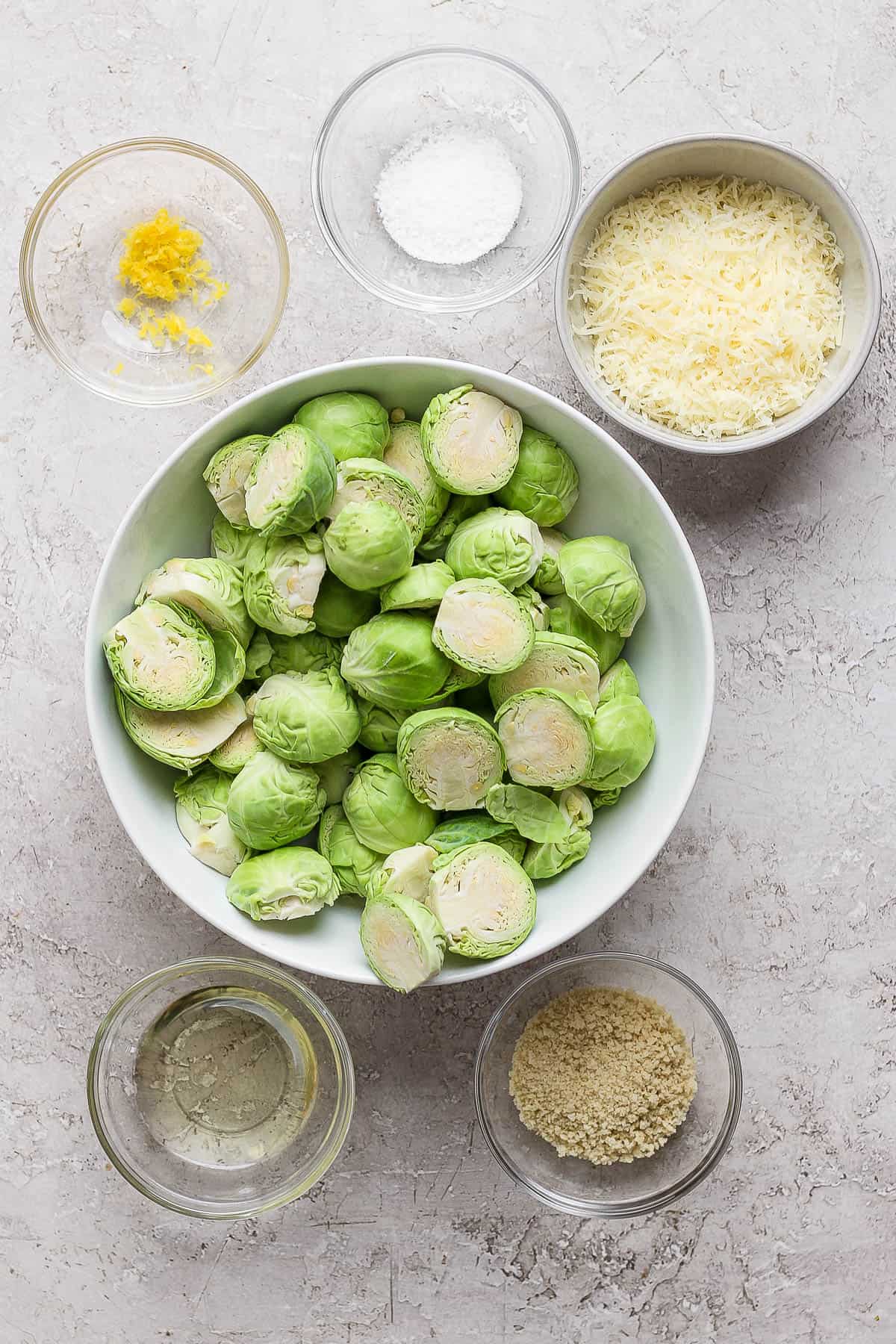 Individual bowls of lemon zest, salt, parmesan cheese, halved brussel sprouts, oil, and panko bread crumbs.