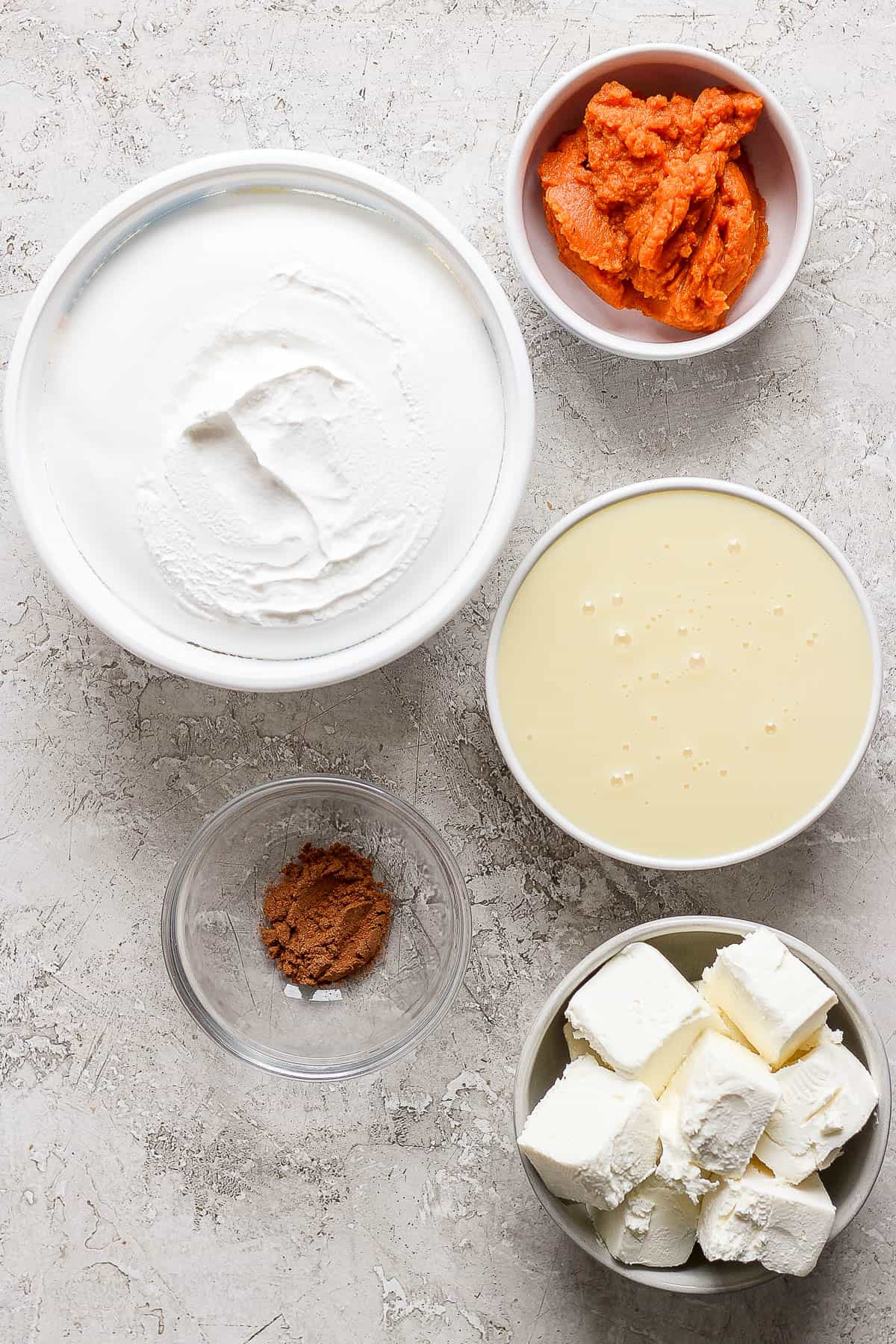 Individual bowls of pumpkin puree, sweetened condensed milk, cool whip, cream cheese, and pumpkin pie spice.