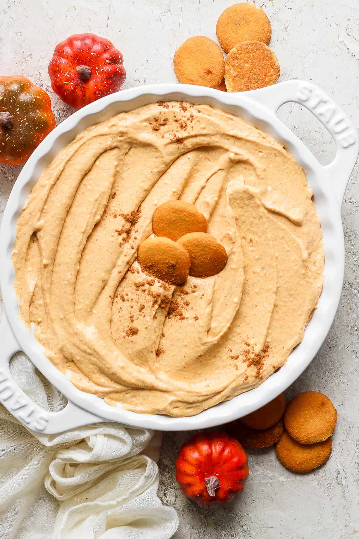 A shallow plate filled with pumpkin dip with three vanilla wafters in the middle sprinkled with cinnamon.