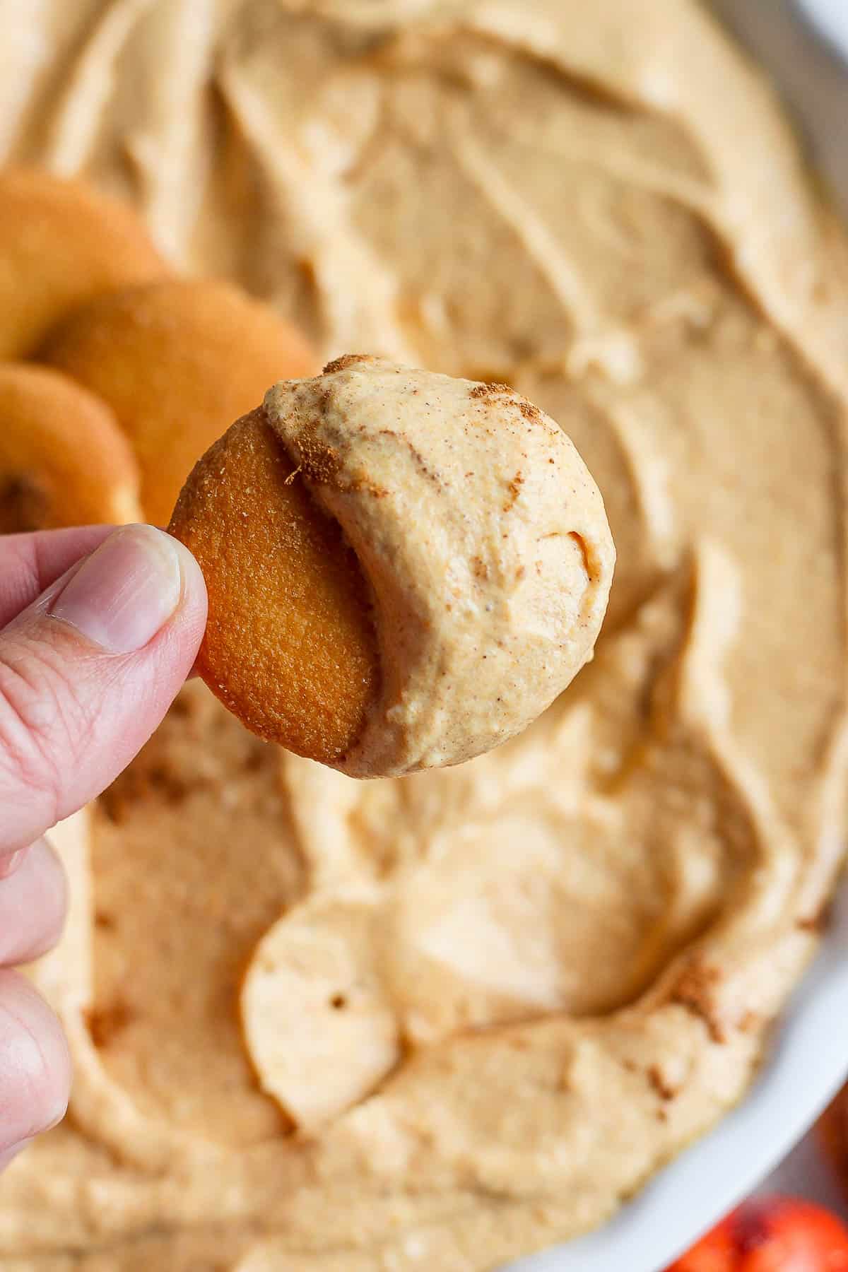 A hand holding a vanilla wafer half covered in pumpkin dip.