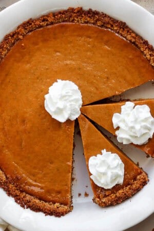 Top down shot of a cooked pumpkin pie in a graham cracker crust with whipped cream on top.