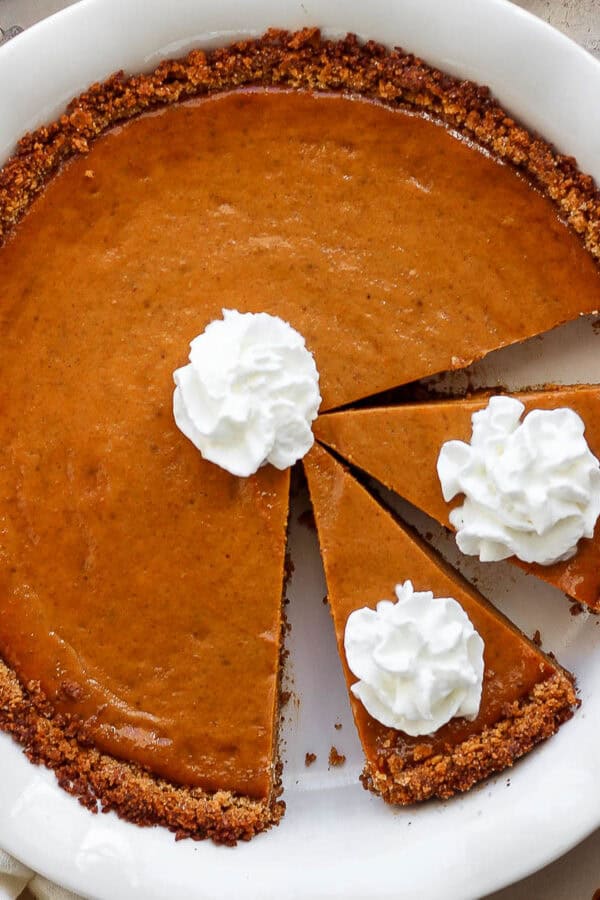 Top down shot of a cooked pumpkin pie in a graham cracker crust with whipped cream on top.