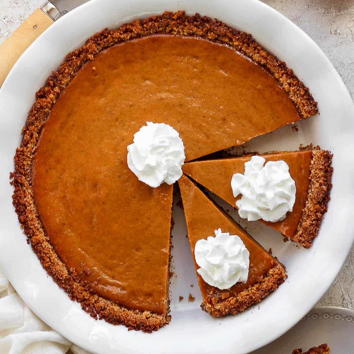 Top down shot of a cooked pumpkin pie in a graham cracker crust with whipped cream on top.