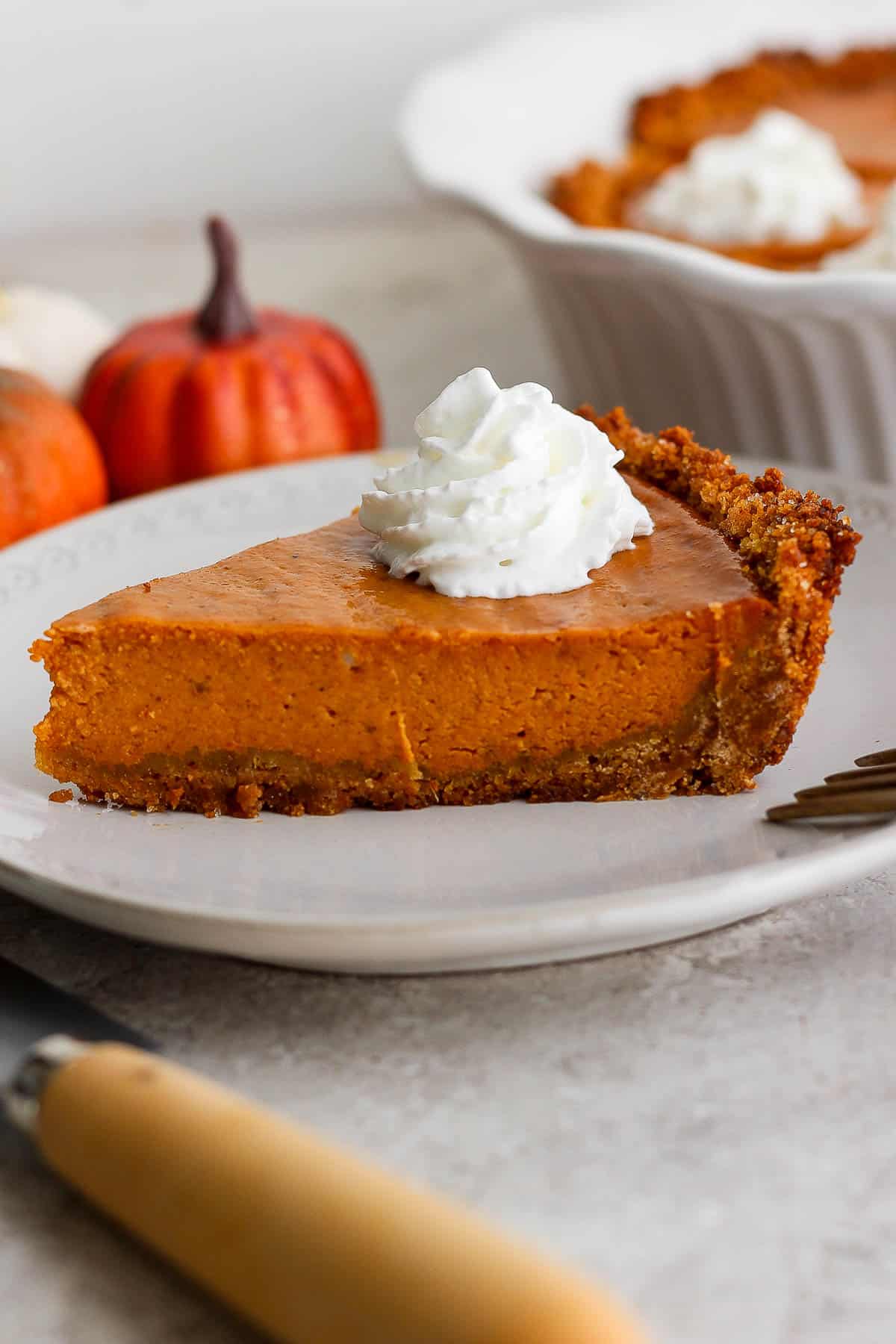 A slice of pumpkin pie with a graham cracker crust on a plate.