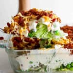 Someone lifting out a piece of seven layer salad out of glass dish.