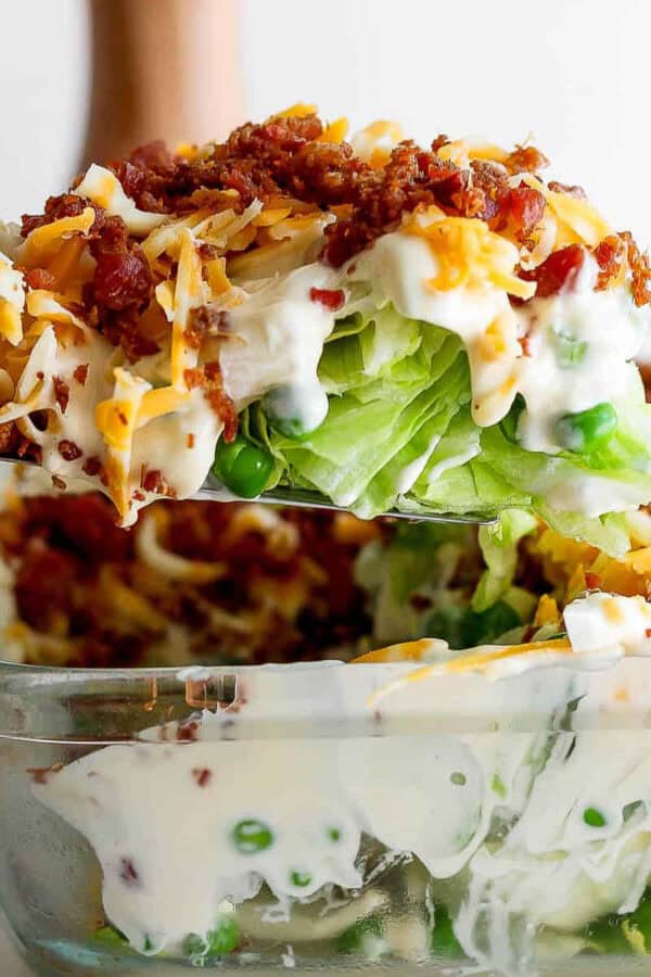 Someone lifting out a piece of seven layer salad out of glass dish.