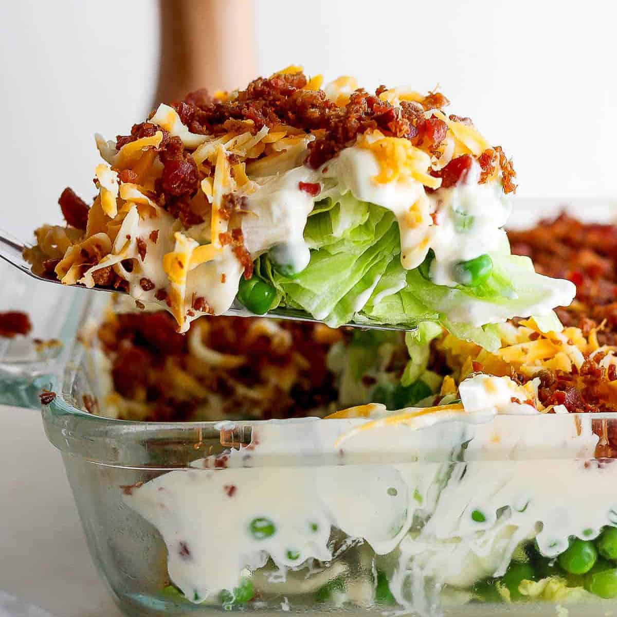 Someone lifting out a piece of seven layer salad out of glass dish.
