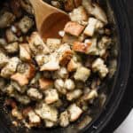 Top down shot of a slow cooker filled with stuffing and a wooden spoon sticking out.