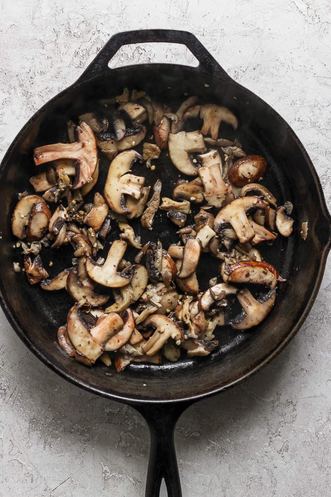 Mushrooms cooking in a cast iron skillet.