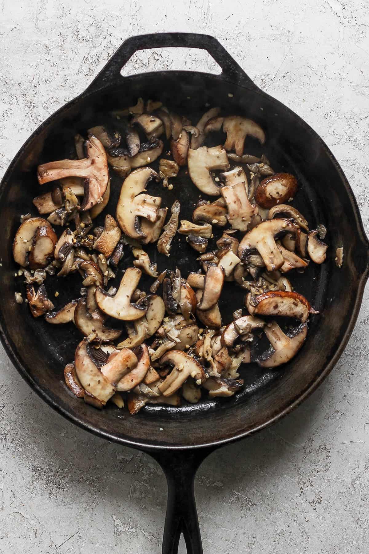 Mushrooms and garlic sautéing in a cast iron skillet with butter.