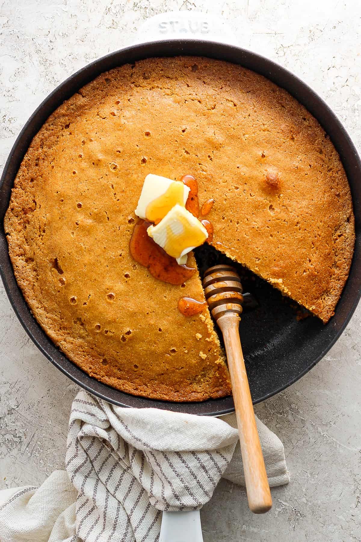 Cooked cornbread in skillet topped with two pats of butter and honey.