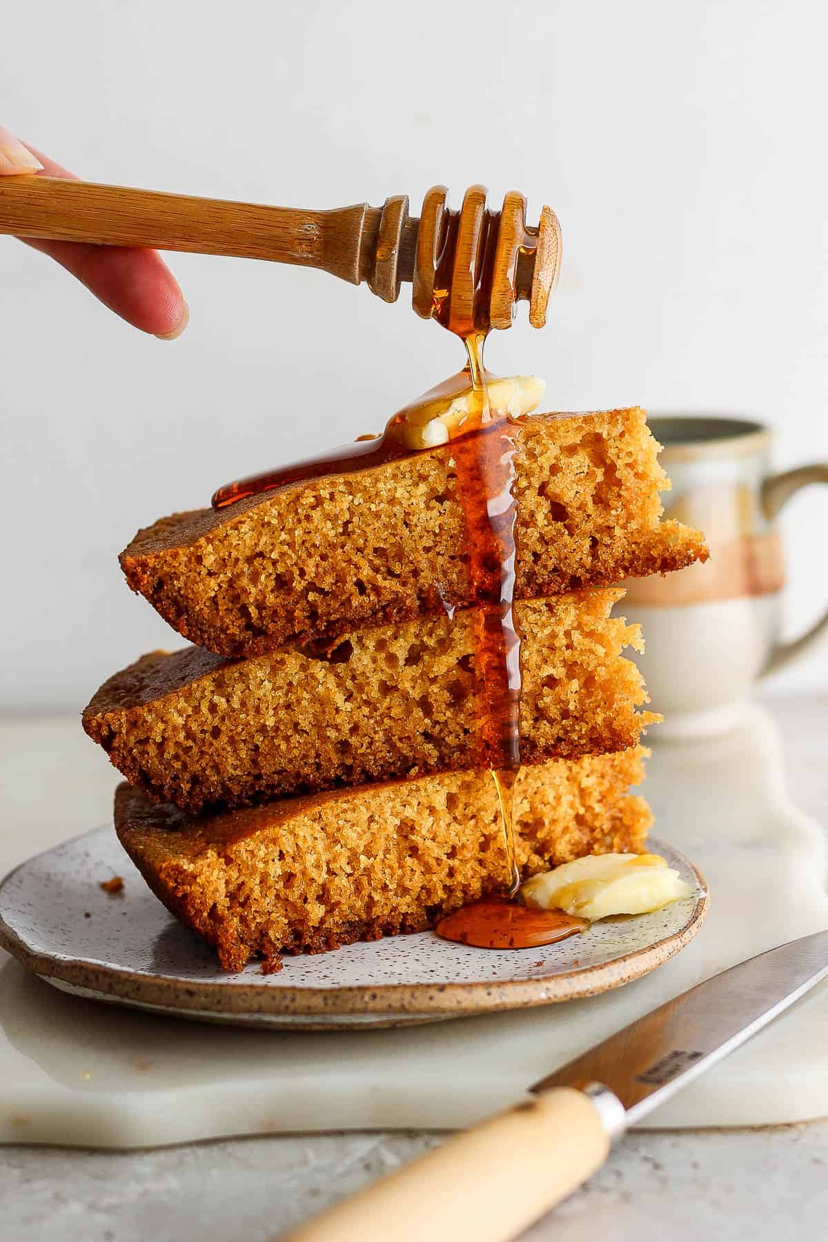 Three slices of cornbread on a plate topped with a pat of butter and dripped with honey.