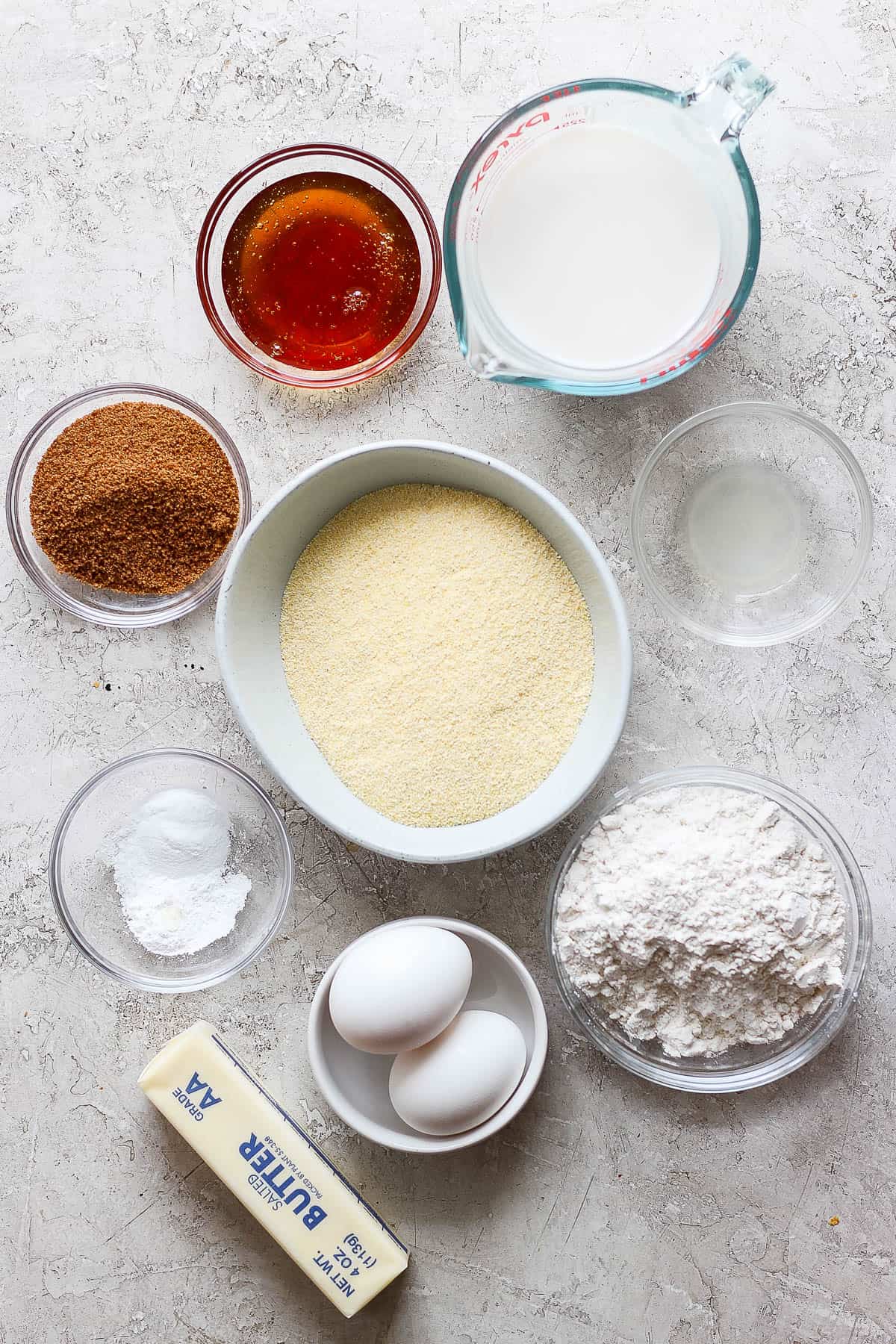 Individual ingredients of milk, cornmeal, honey, lemon juice, coconut sugar, eggs, butter, and baking powder.