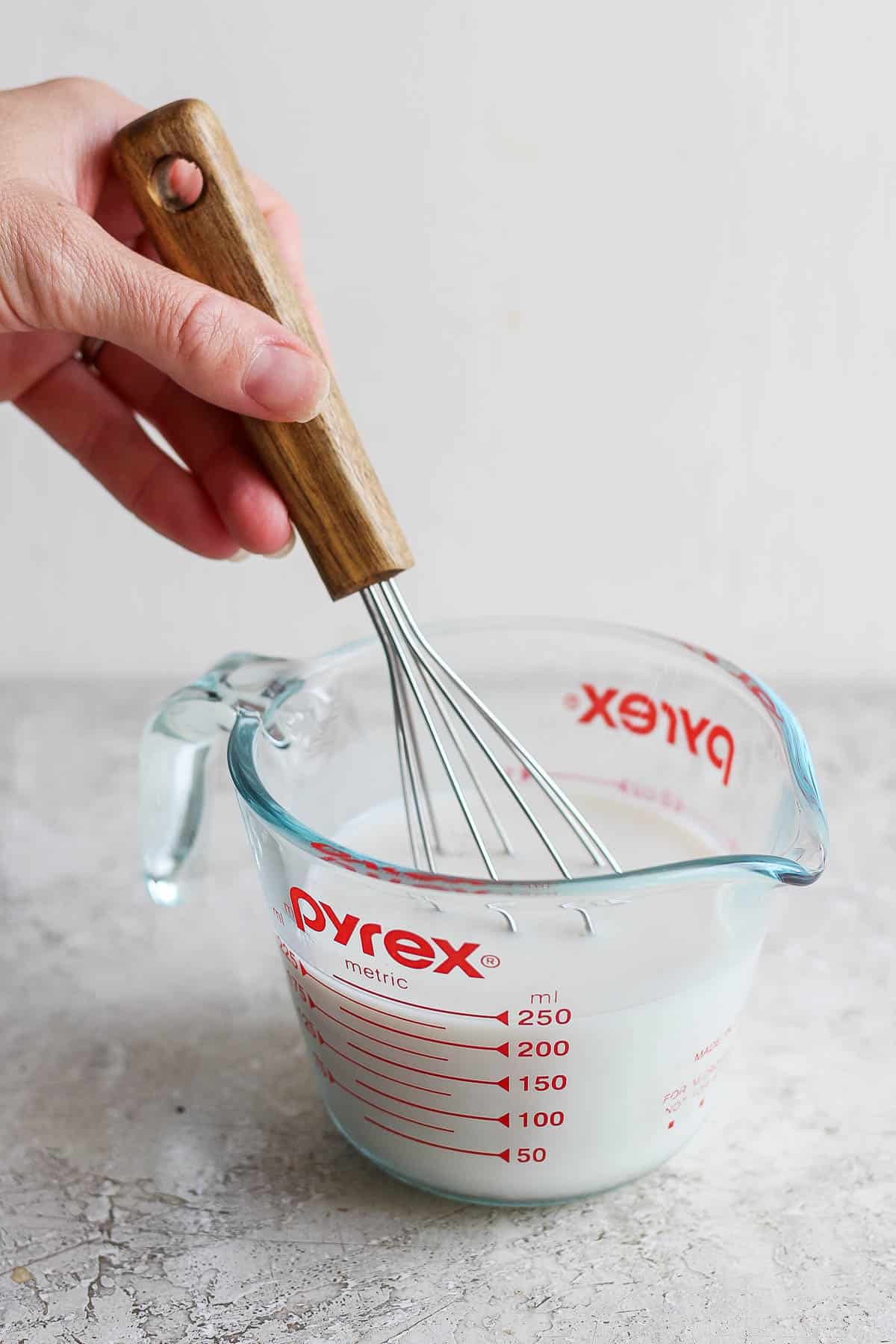 A whisk in a measuring cup with milk and lemon.