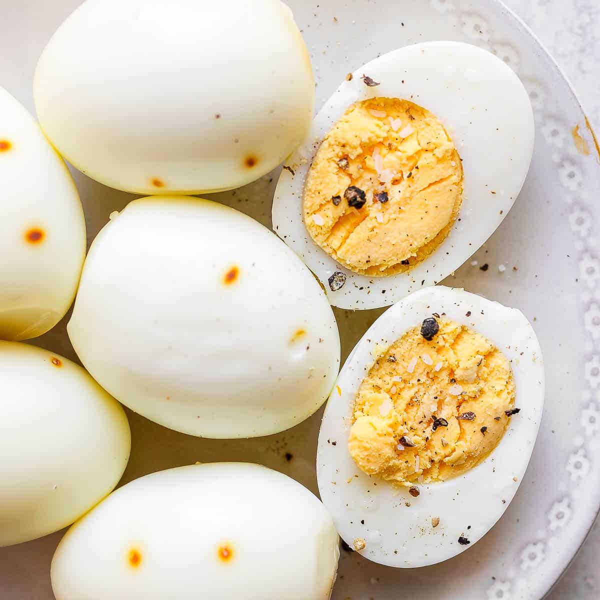 A top down shot of a plate of smoked eggs with one cut open to show the cooked inside with salt and pepper on top.