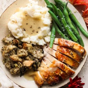 A plate of mashed potatoes with smoked turkey gravy on top, green beans, stuffing and turkey.