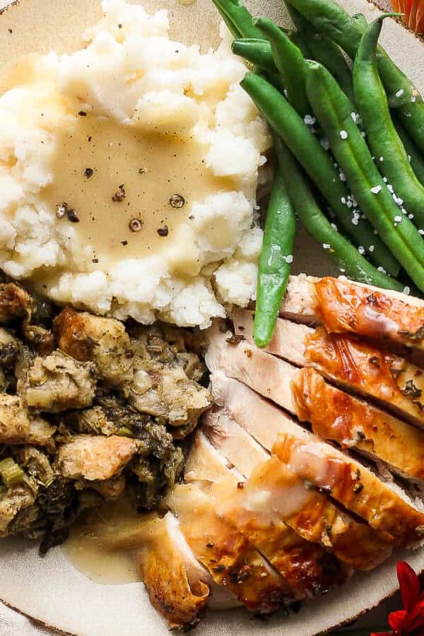 A plate of mashed potatoes with smoked turkey gravy on top, green beans, stuffing and turkey.