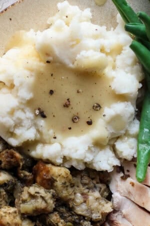 A plate with turkey, green beans, stuffing a mashed potatoes with smoked turkey gravy on top.