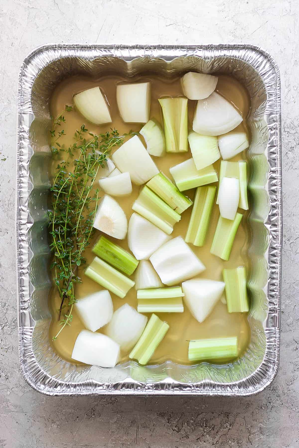 A large roasting pan with rosemarry, quartered onions, celery, and turkey drippings. 