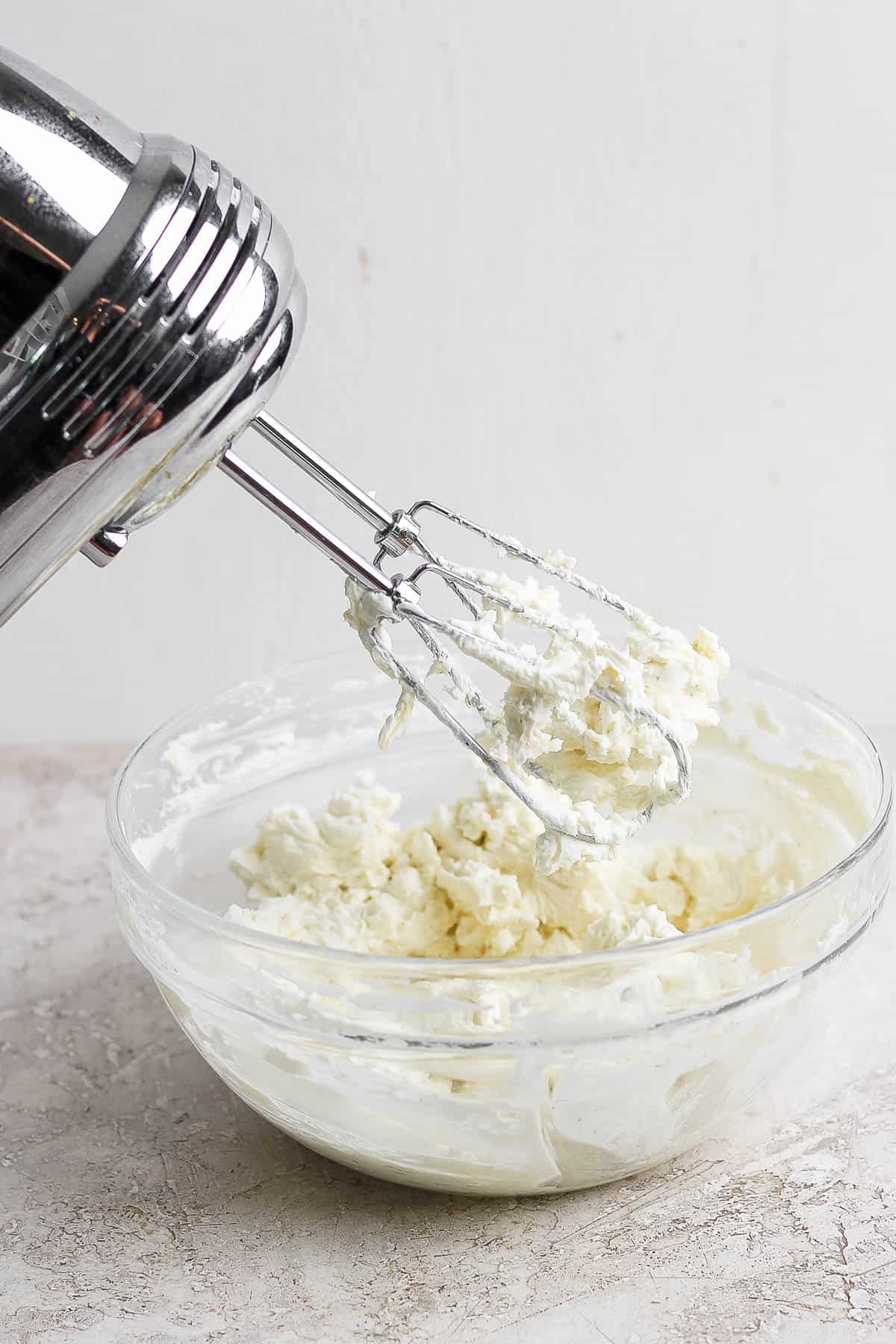 Baked goat cheese dip ingredients blended with a hand mixer in a large bowl.