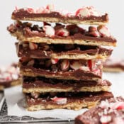 A stack of peppermint christmas crack pieces on piece of parchment with crushed candy canes on top.