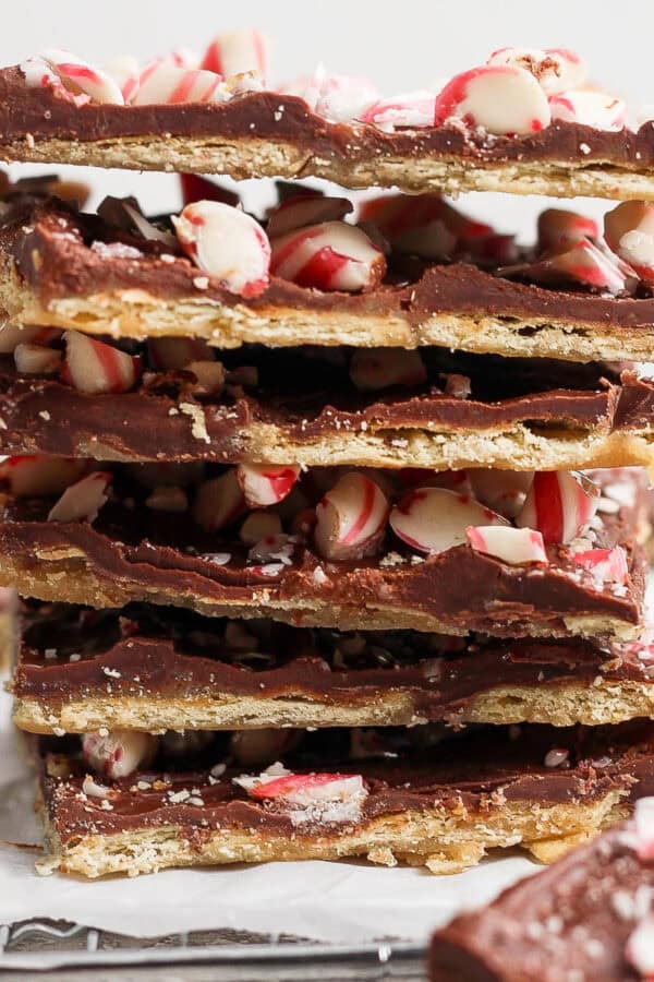 A stack of peppermint christmas crack pieces on piece of parchment with crushed candy canes on top.