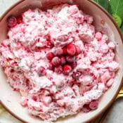A bowl of cranberry fluff salad with frozen cranberries on top and fresh bay leaves next to the bowl.