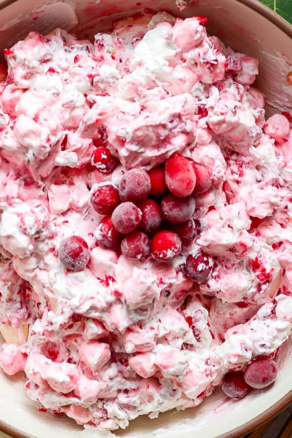 A bowl of cranberry fluff salad with frozen cranberries on top and fresh bay leaves next to the bowl.