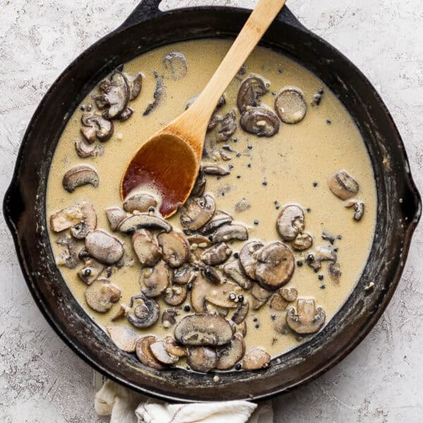 Top down shot of a cast iron skillet with creamy mushroom sauce inside and a wooden spoon sticking out.