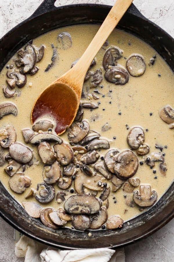 Top down shot of a cast iron skillet with creamy mushroom sauce inside and a wooden spoon sticking out.