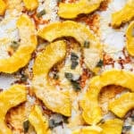 Roasted delicata squash on a parchment-lined baking sheet with shredded parmesan cheese and sage.