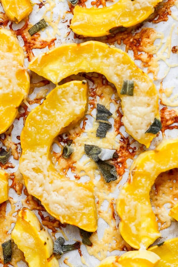 Roasted delicata squash on a parchment-lined baking sheet with shredded parmesan cheese and sage.