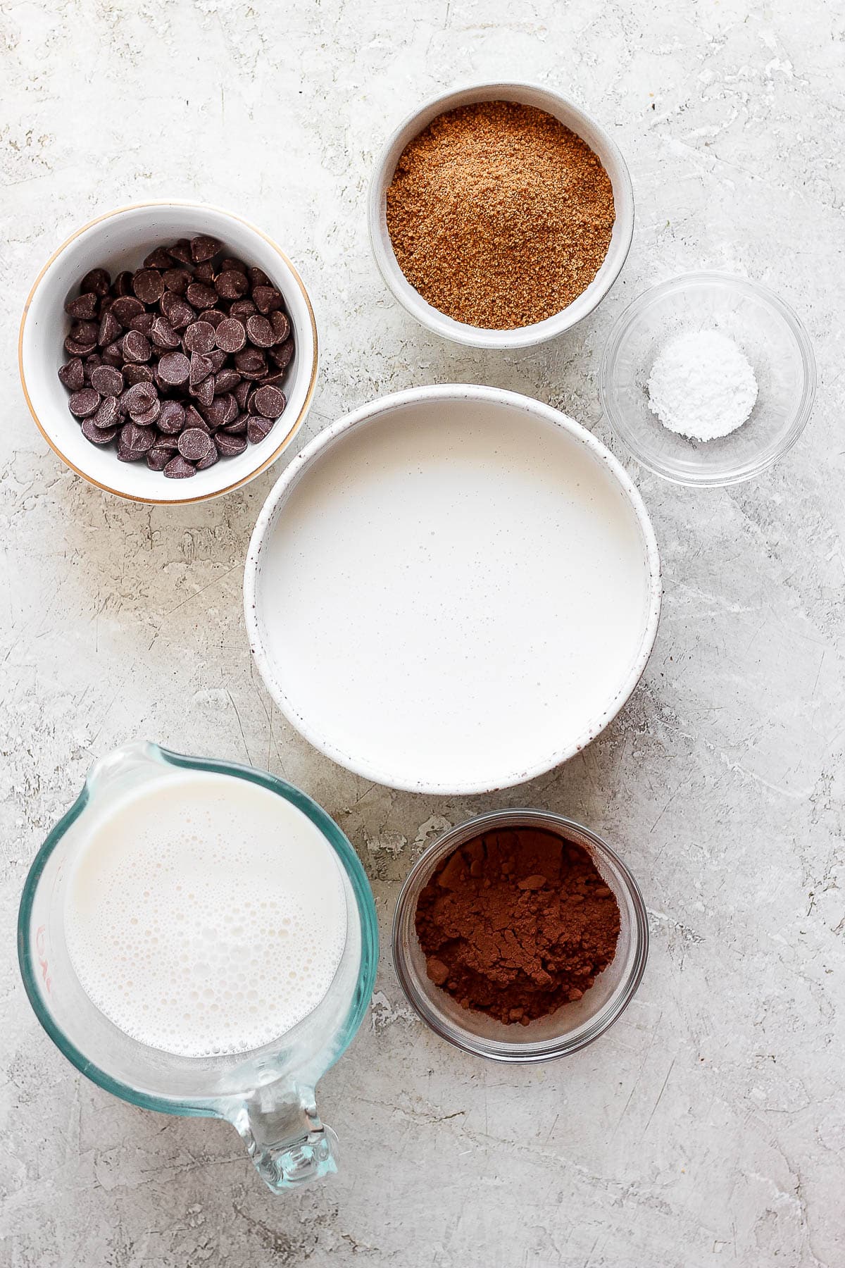 Individual bowls of chocolate chips, cocoa powder, whole milk, heavy whipping cream, salt, and sugar.