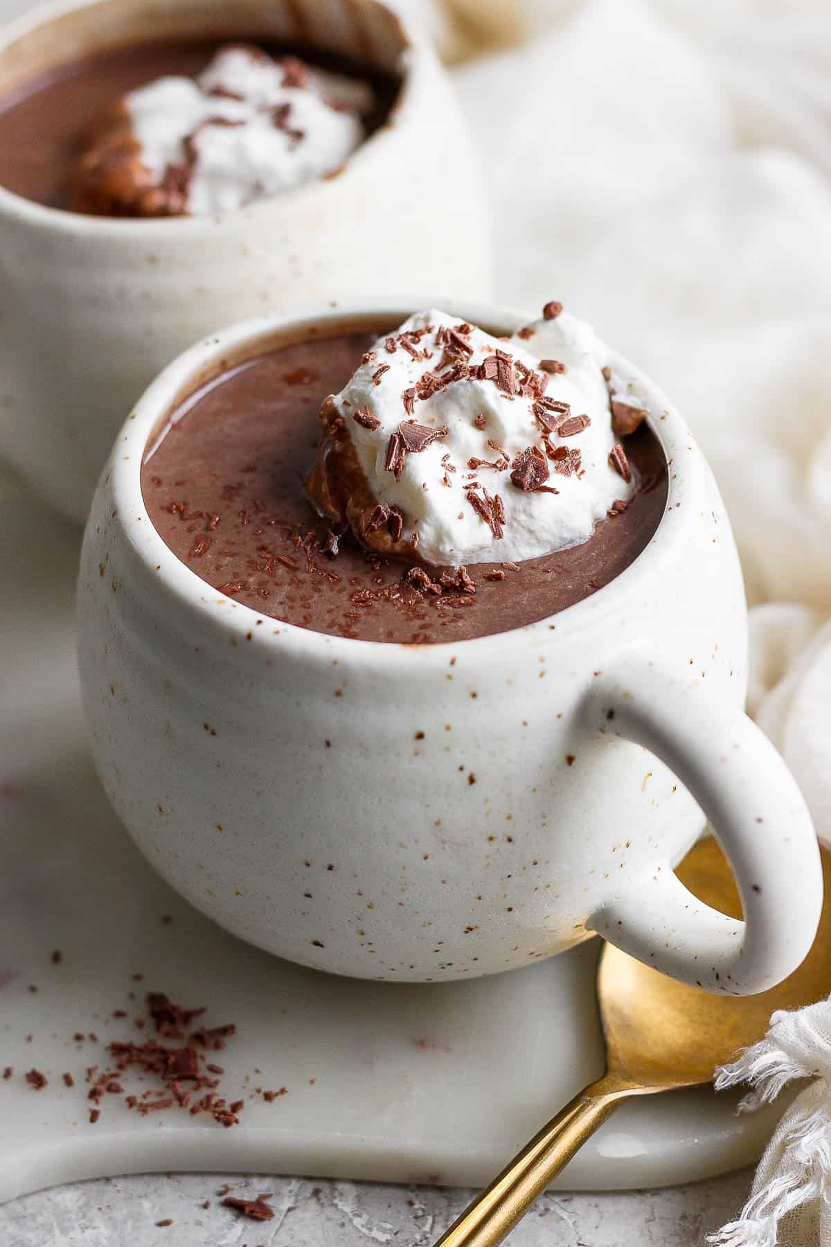 A cup full of hot chocolate topped with whipped cream and shaved chcolate.