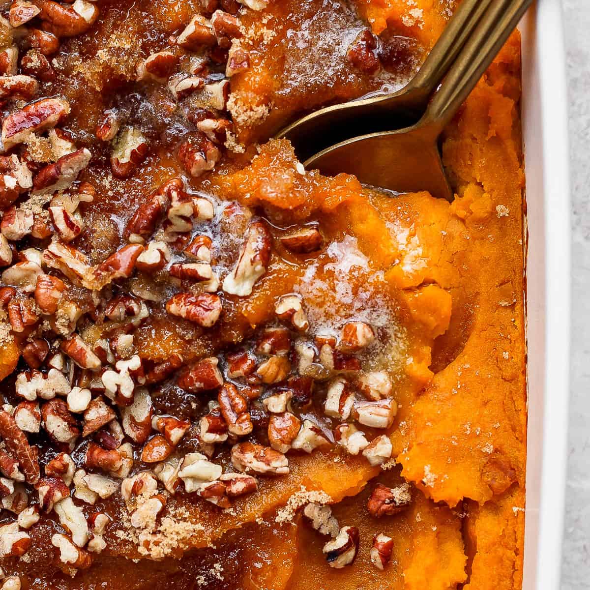 Top down close up shot of a squash casserole with pecans, brown sugar and a spoon sticking out.