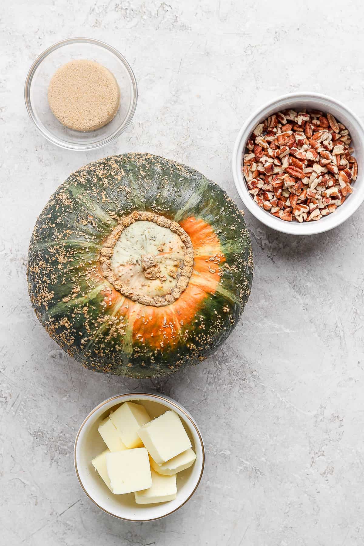 A whole butternut squash, and individual bowls of chopped pecans, butter, and brown sugar.