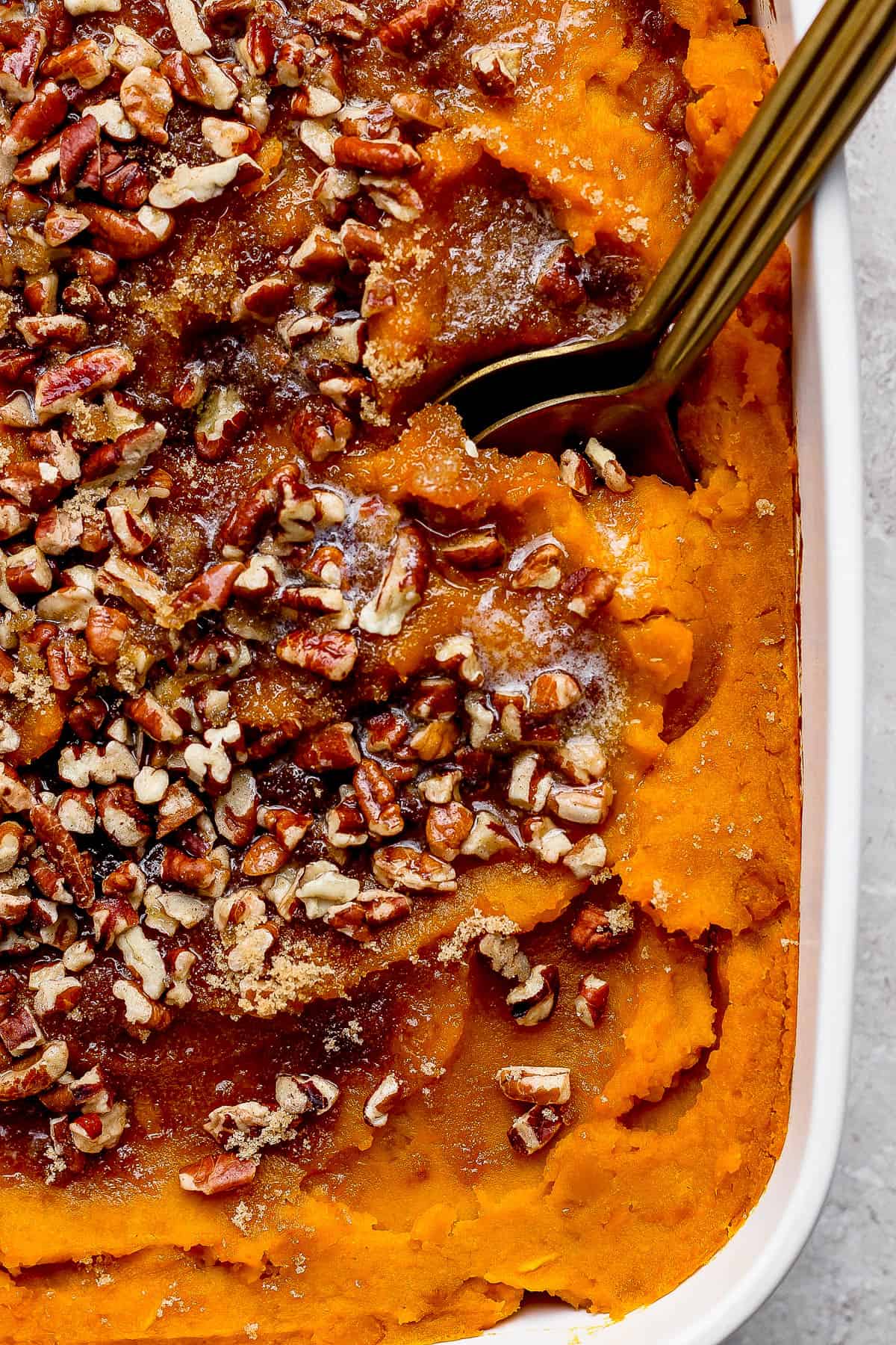 Butternut squash casserole topped with pecans with two spoons stuck into the casserole dish.