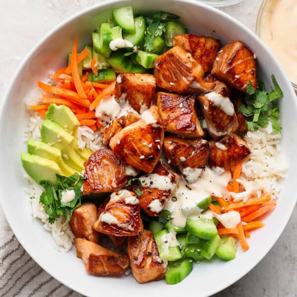 A bowl filled with rice, avocado, carrots, cucumber, bang bang salmon and spicy mayo.