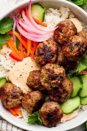 A Banh Mi Rice Bowl with rice, pork meatballs, pickled vegetables, cucumbers and spicy mayo.