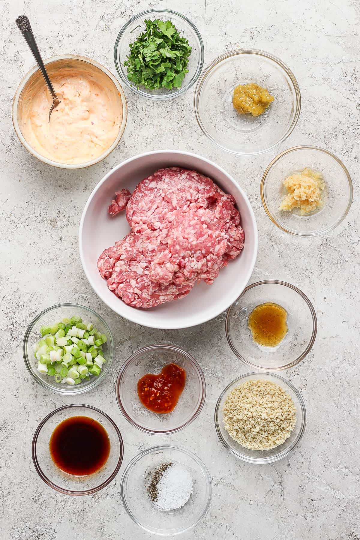 Individual bowls of spicy mayo, cilantro, lemongrass paste, minced garlic, ground pork, fish sauce, soy sauce, scallions, bread crumbs, garlic chili sauce, salt, and pepper.