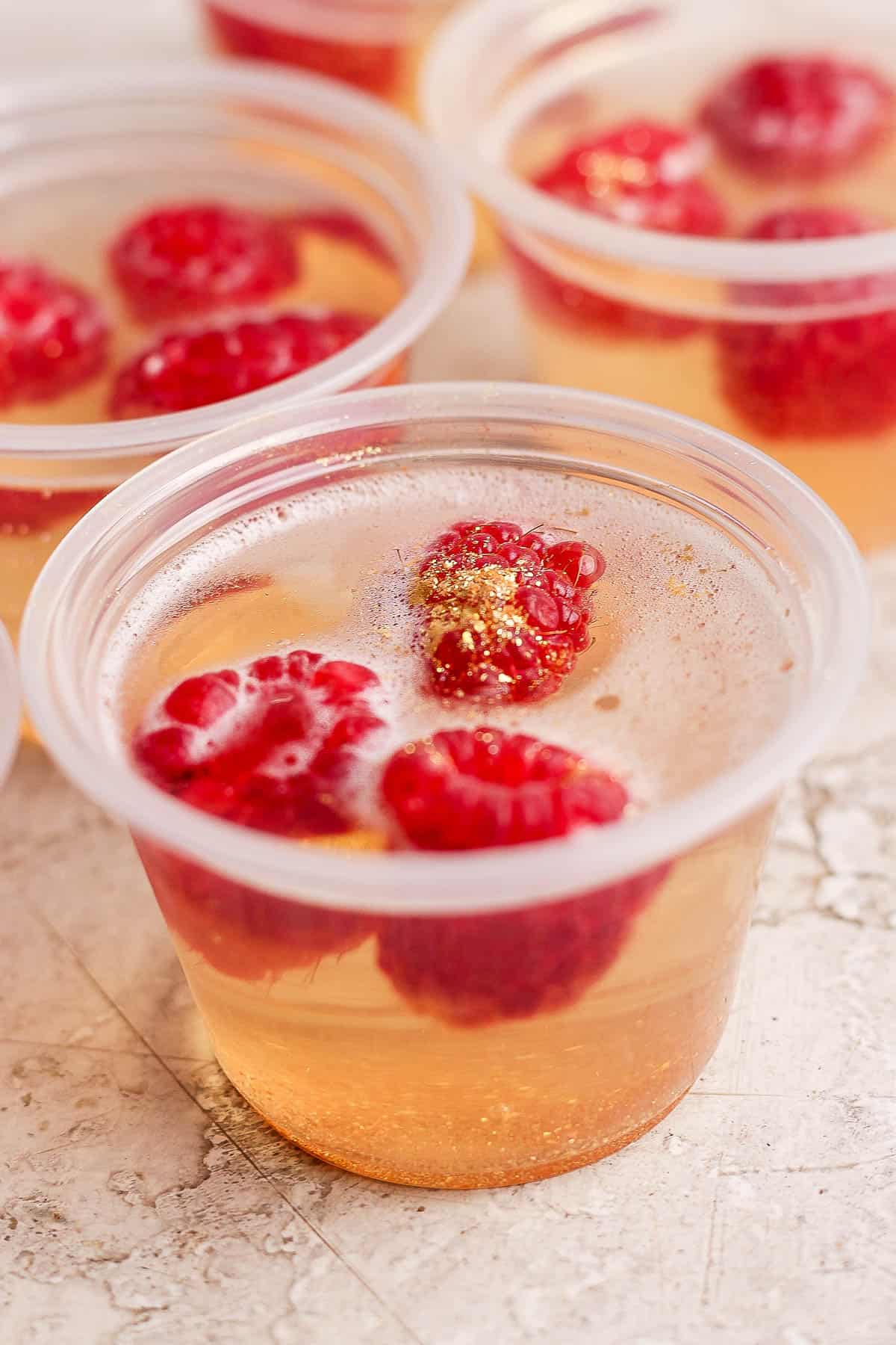 A filled portion cup with raspberries, glitter, and the gelatin mixture.