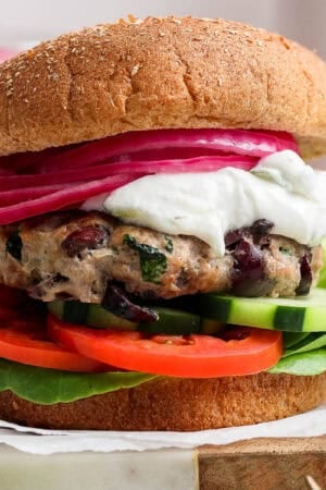 A greek turkey burger on a whole wheat bun with lettuce, tomato, cucumber, tzatziki and pickled onions.